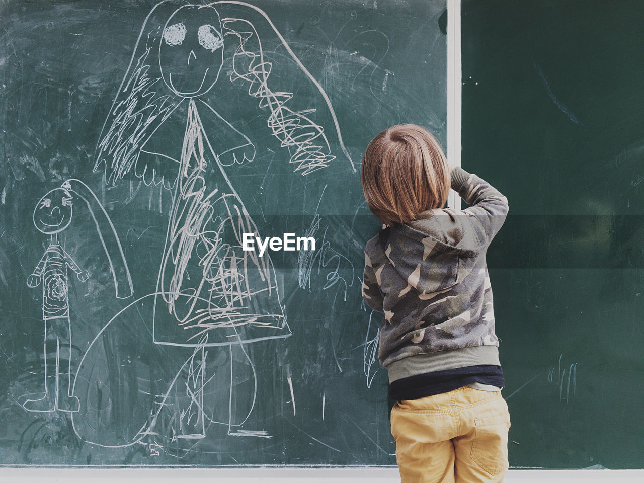 Rear view of boy drawing on blackboard at classroom
