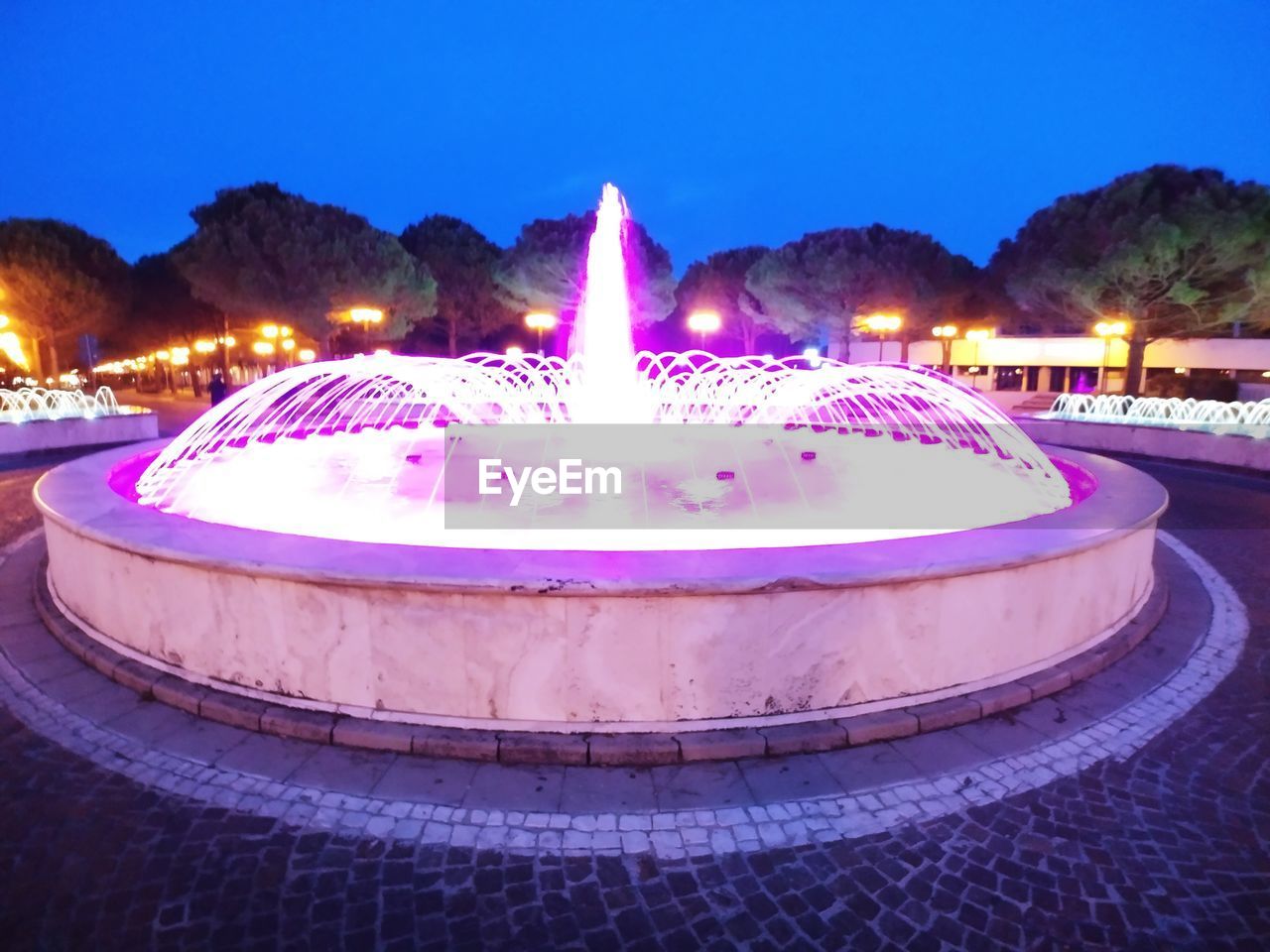 PANORAMIC VIEW OF ILLUMINATED FOUNTAIN AT NIGHT