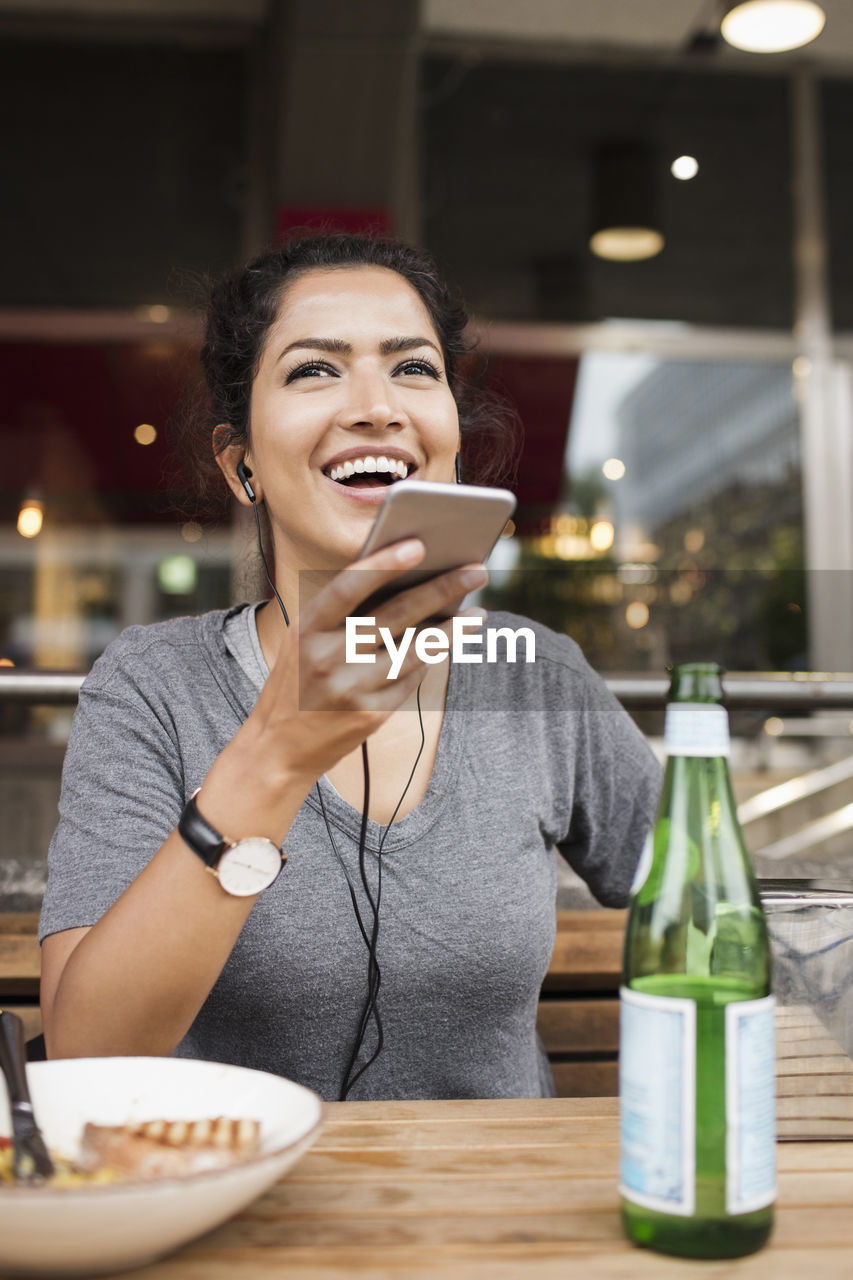 Happy woman using mobile phone while sitting at sidewalk cafe