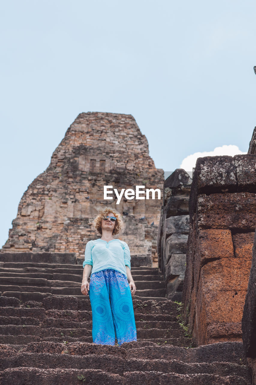 Low angle portrait of woman standing at historical building against sky