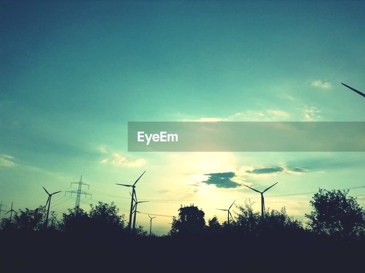 Silhouette of wind turbines and power lines at sunset