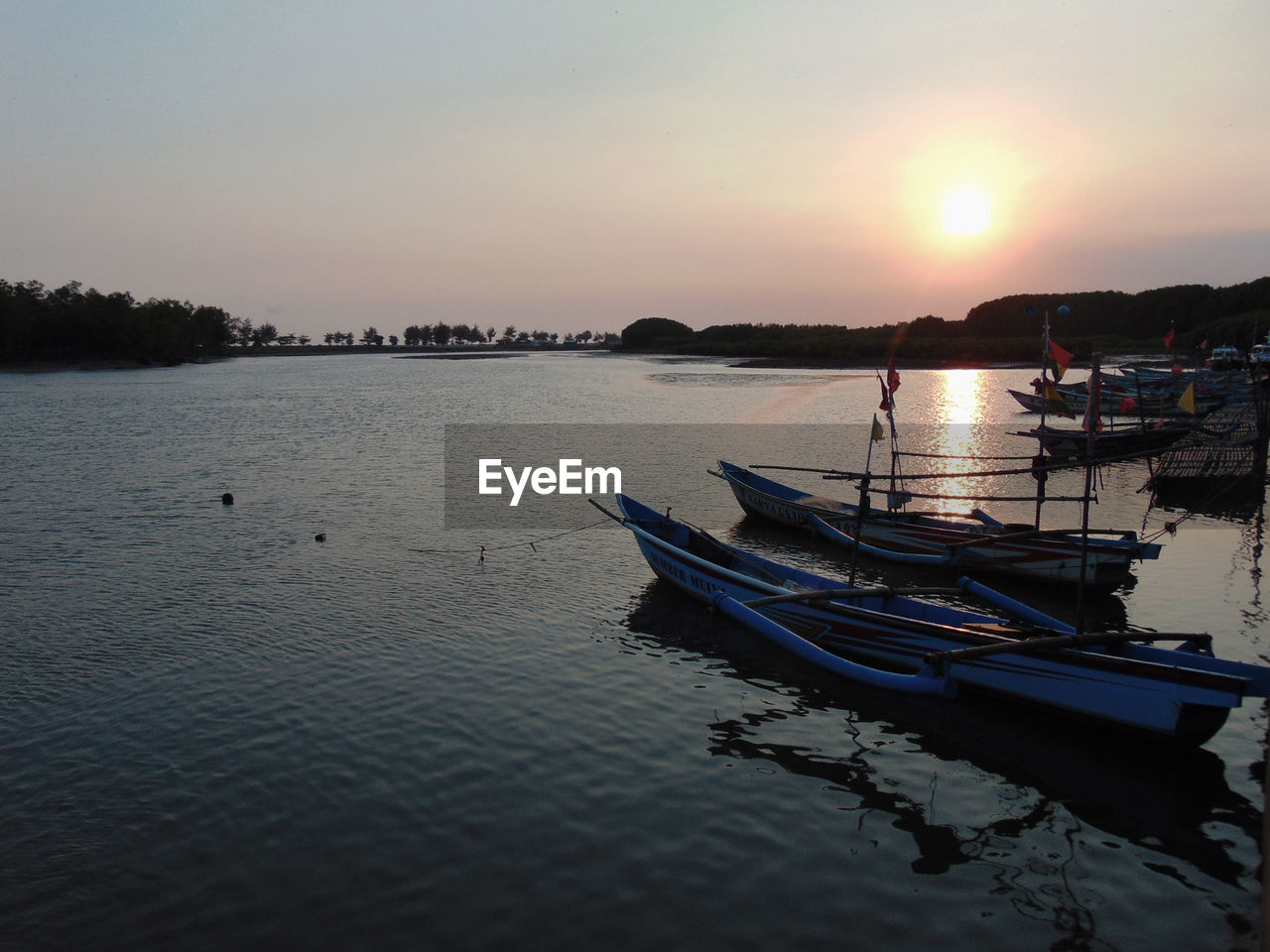 Boat moored in lake against sky during sunset