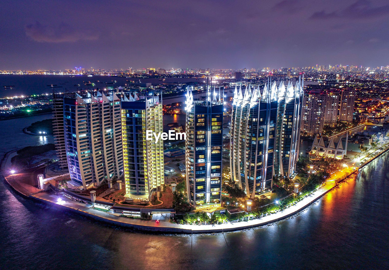 Illuminated buildings by river against sky at night