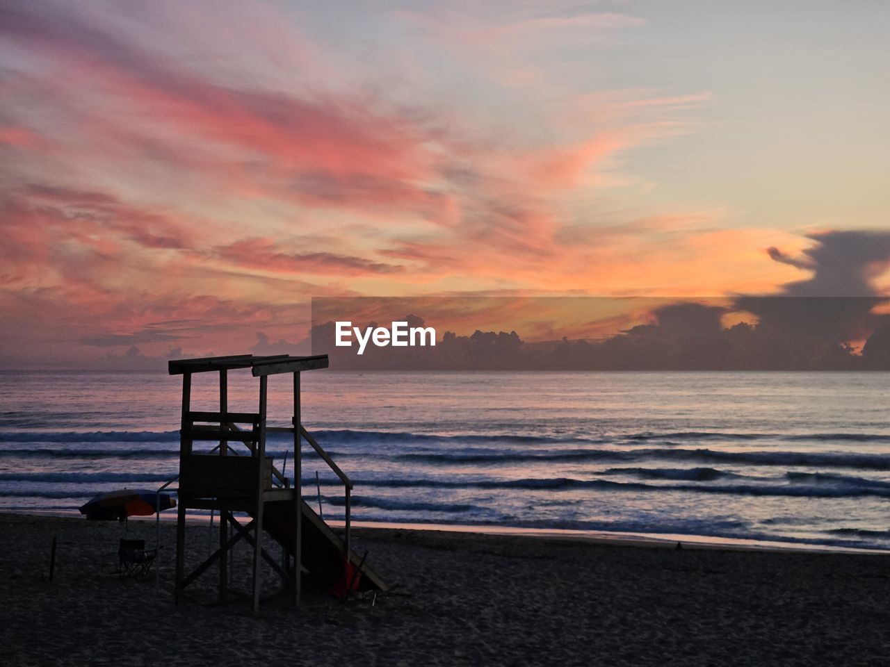 sky, sea, water, beach, land, sunset, cloud, beauty in nature, ocean, nature, horizon, scenics - nature, lifeguard hut, tranquility, shore, tranquil scene, lifeguard, horizon over water, coast, hut, sand, dawn, architecture, no people, evening, man made structure, body of water, outdoors, idyllic, orange color, travel destinations, wave, built structure, chair, holiday, dramatic sky, vacation, trip, seat, sun, silhouette