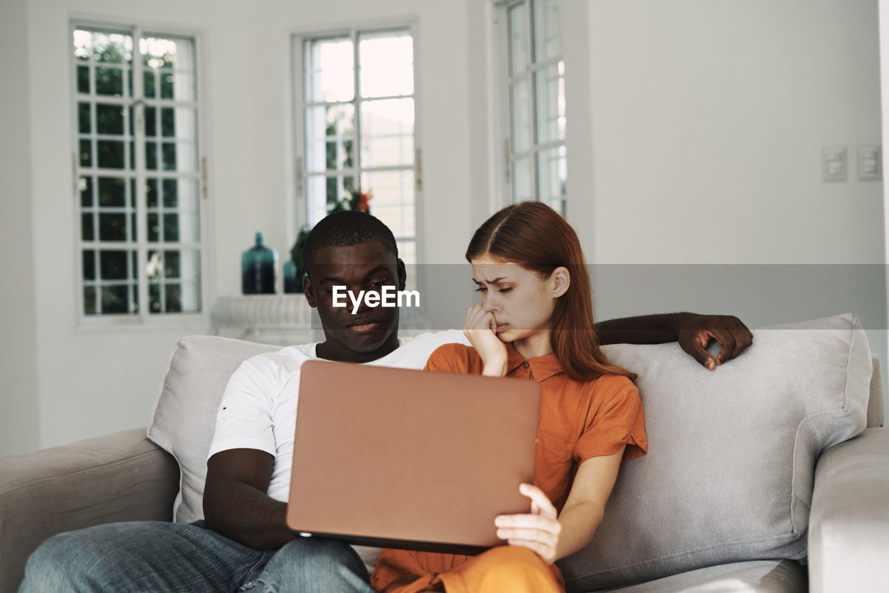 Couple using laptop while sitting on sofa at home