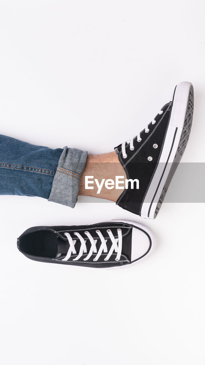 Low section of man wearing canvas shoe against white background