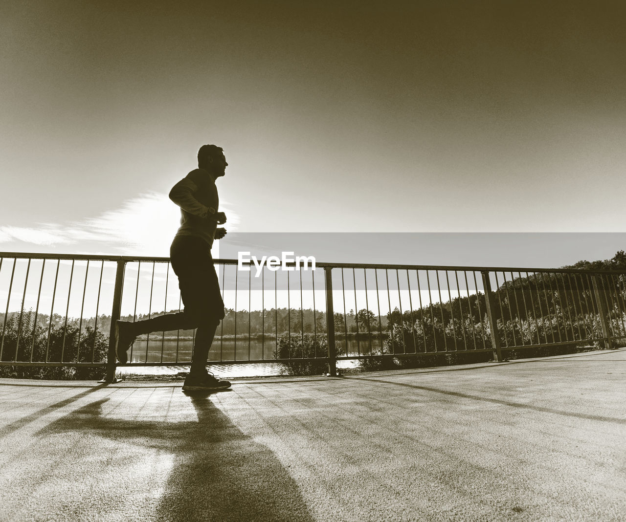 Man running quickly on shore bridge. silhouette of runner exercising and stretching on lake street