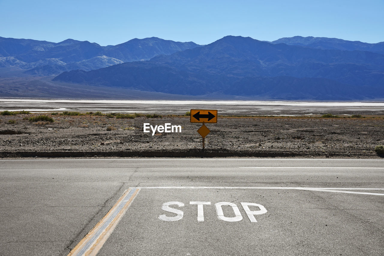 Stop text on road by mountains against clear sky