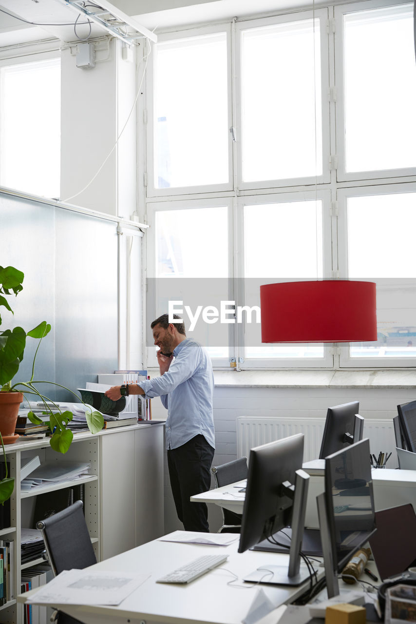 Businessman talking on phone while reading document at creative office