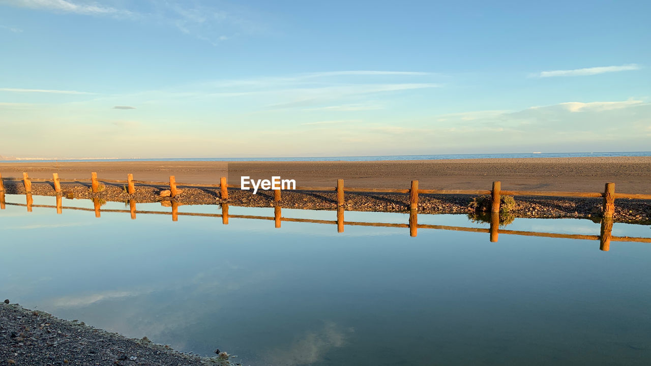 WOODEN POSTS ON BEACH AGAINST SKY
