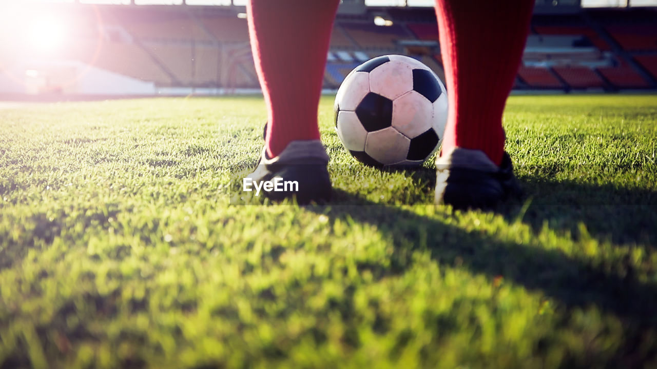 Low section of man playing soccer at stadium on sunny day