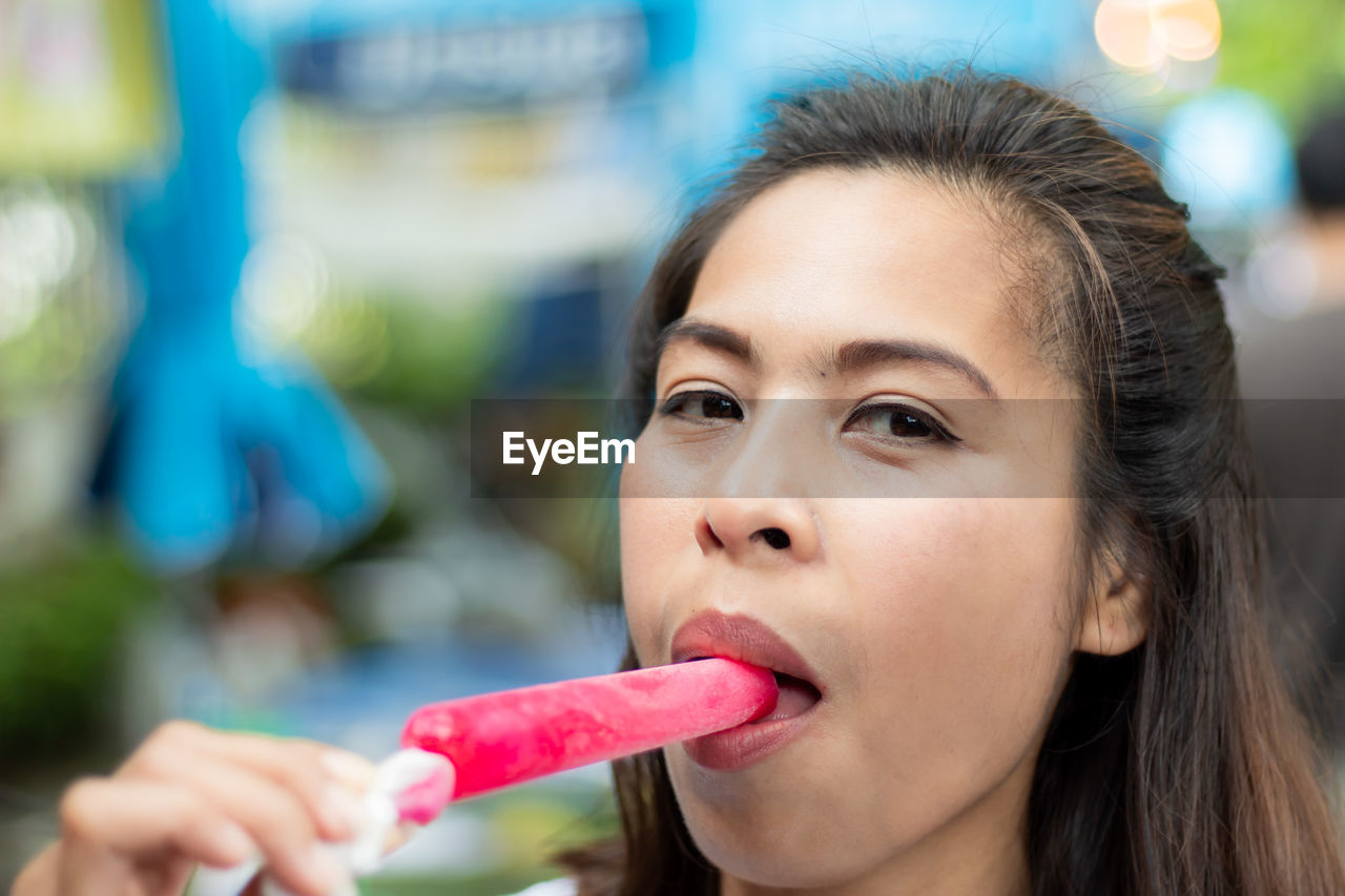 Close-up portrait of woman having pink popsicle outdoors