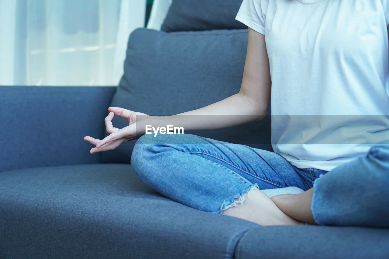 LOW SECTION OF WOMAN SITTING AT SOFA