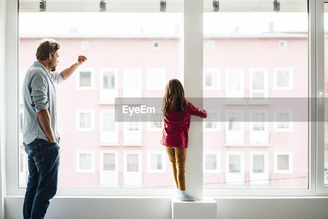 Daughter and father standing by window at home