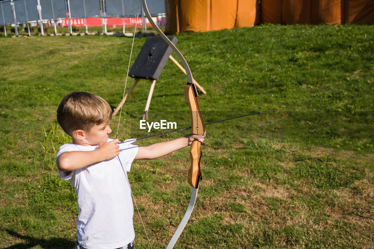 Boy aiming bow while standing outdoor