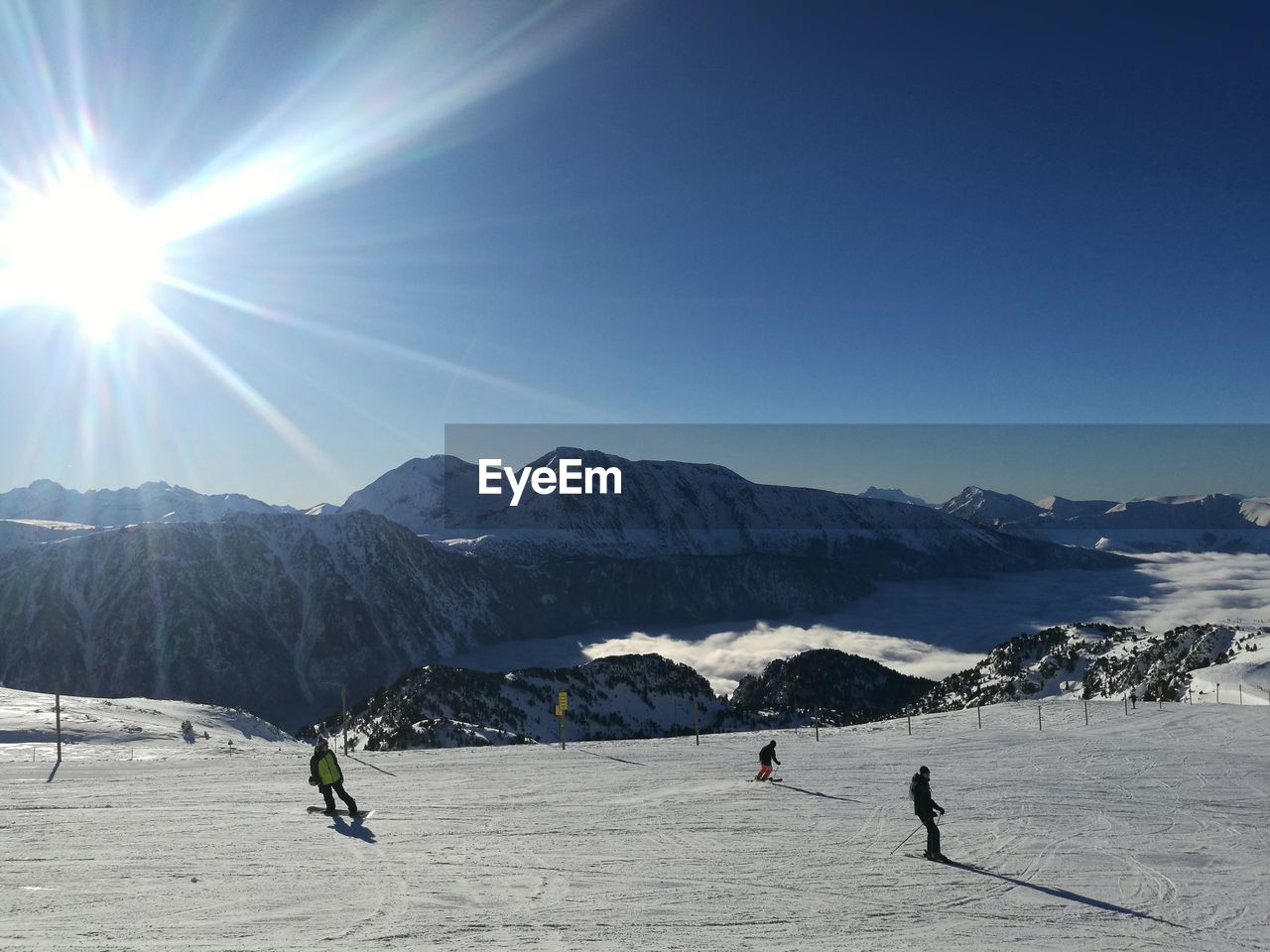 People skiing on snow by mountains against blue sky