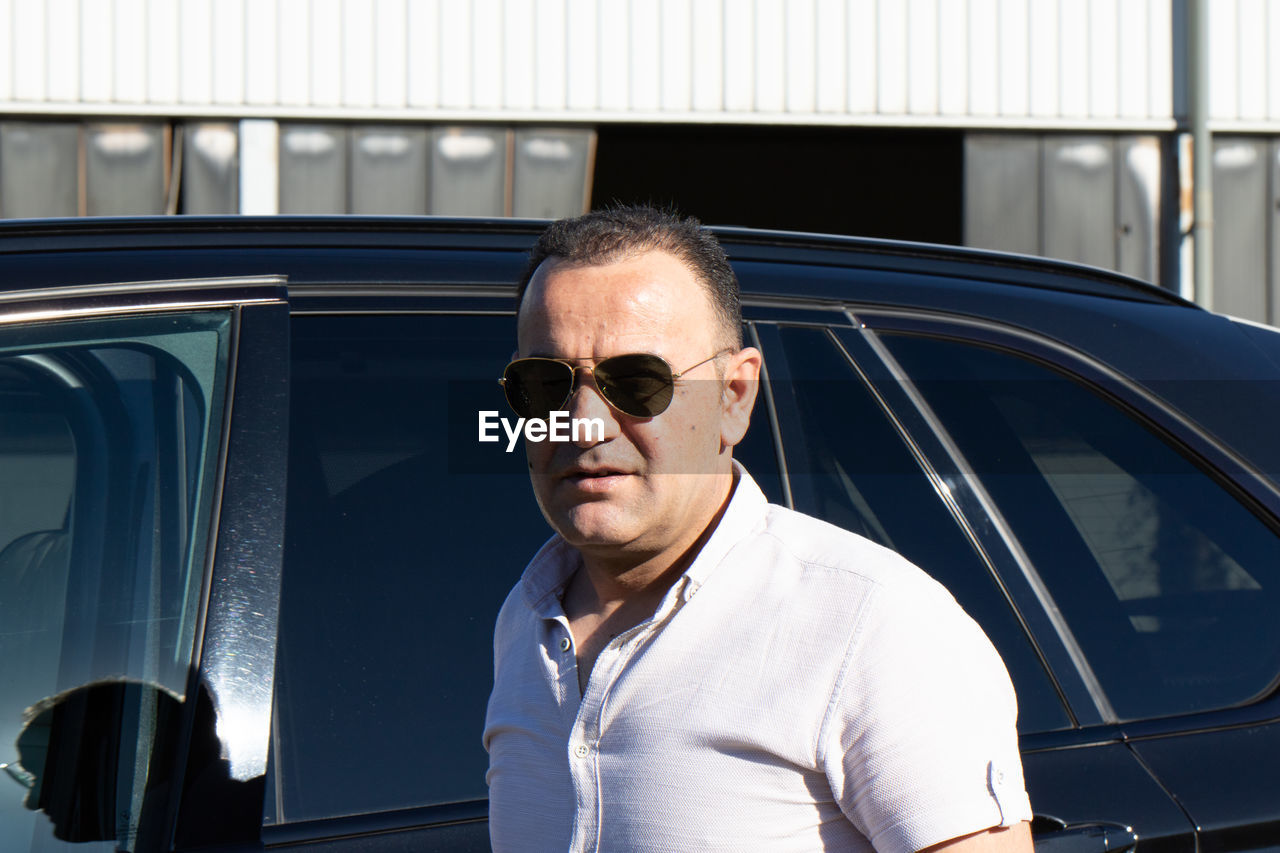 Portrait of man wearing sunglasses standing by car