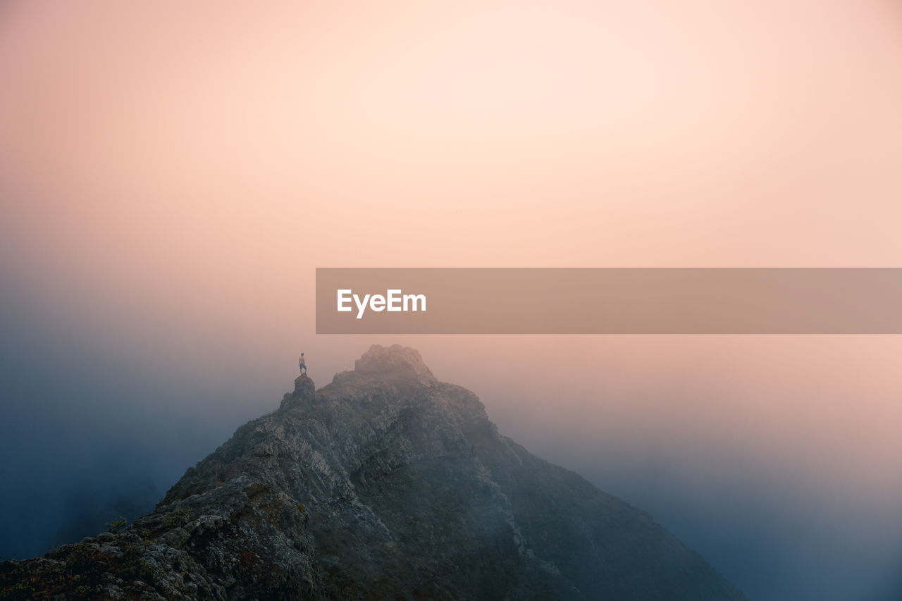 Distant view of explorer standing on mountain ridge on foggy morning during vacation in tenerife