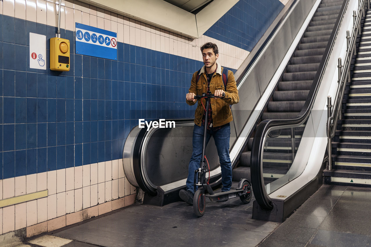 Man in stylish outfit walking with electric scooter in the underground