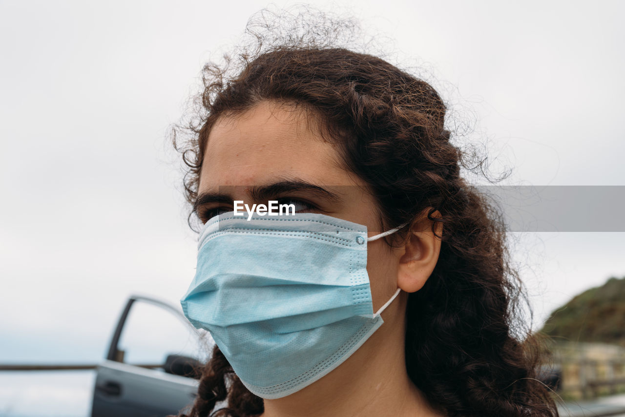 Portrait of a beautiful young woman wearing face mask against sky