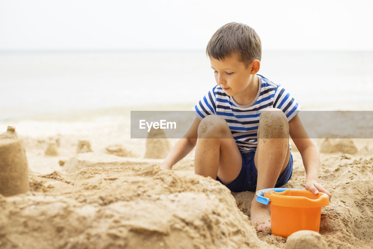 side view of boy sitting on sand at beach