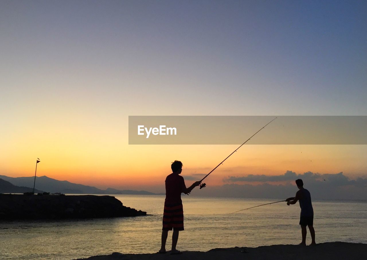 Silhouette men fishing in sea against clear sky