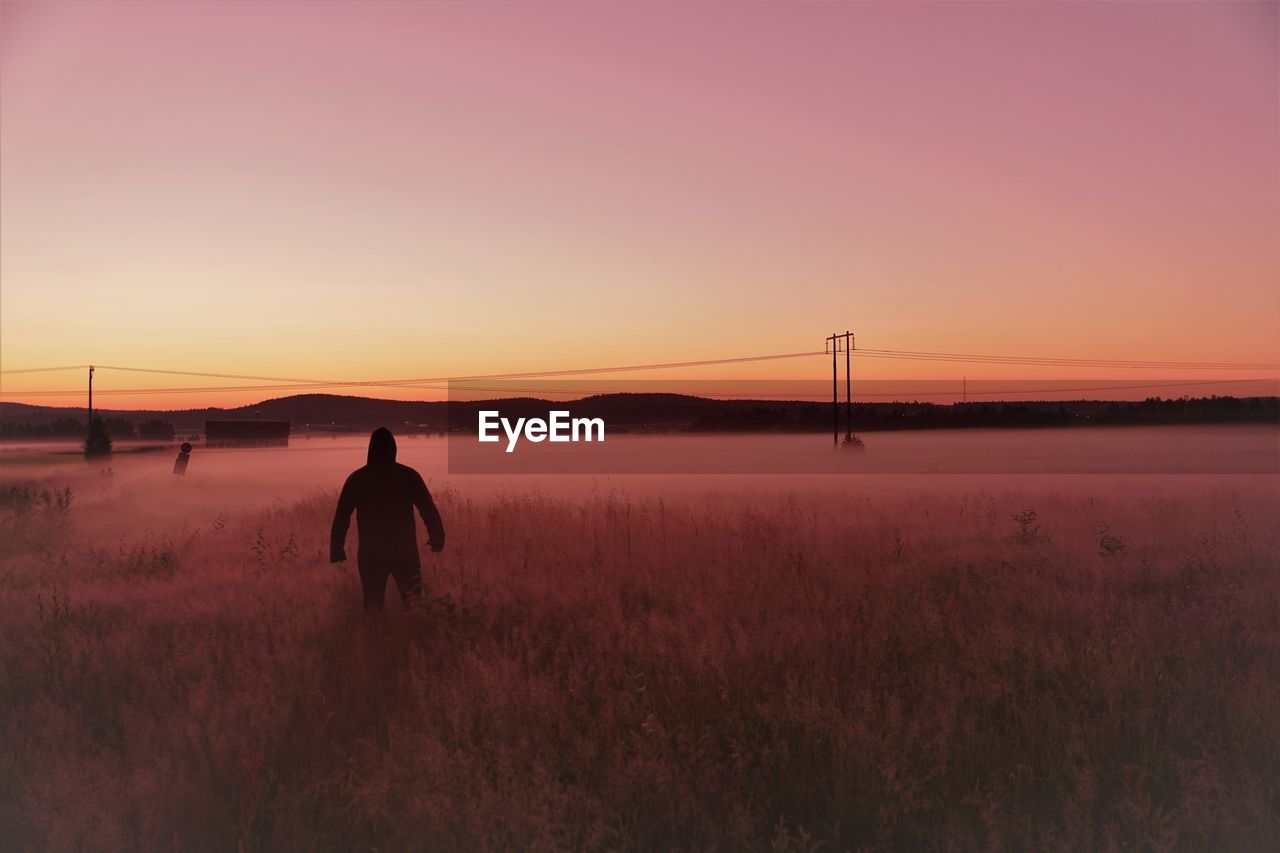 Rear view of man standing on field against sky during sunset