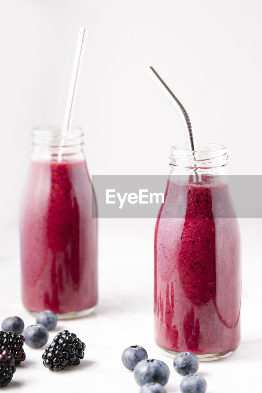 Berry smoothie on glass bottles on a white marble surface. vertical image.