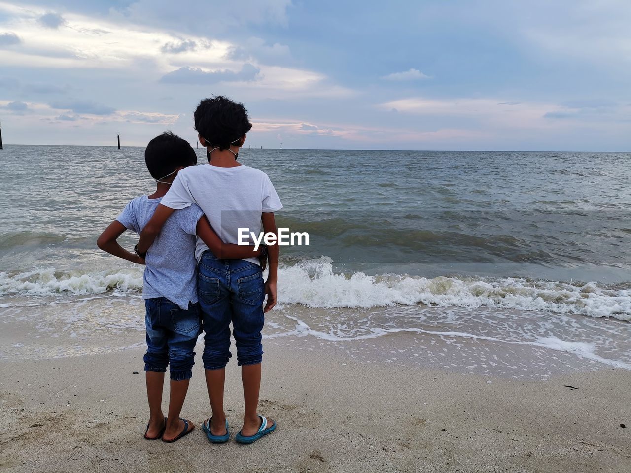 REAR VIEW OF BOYS STANDING ON BEACH