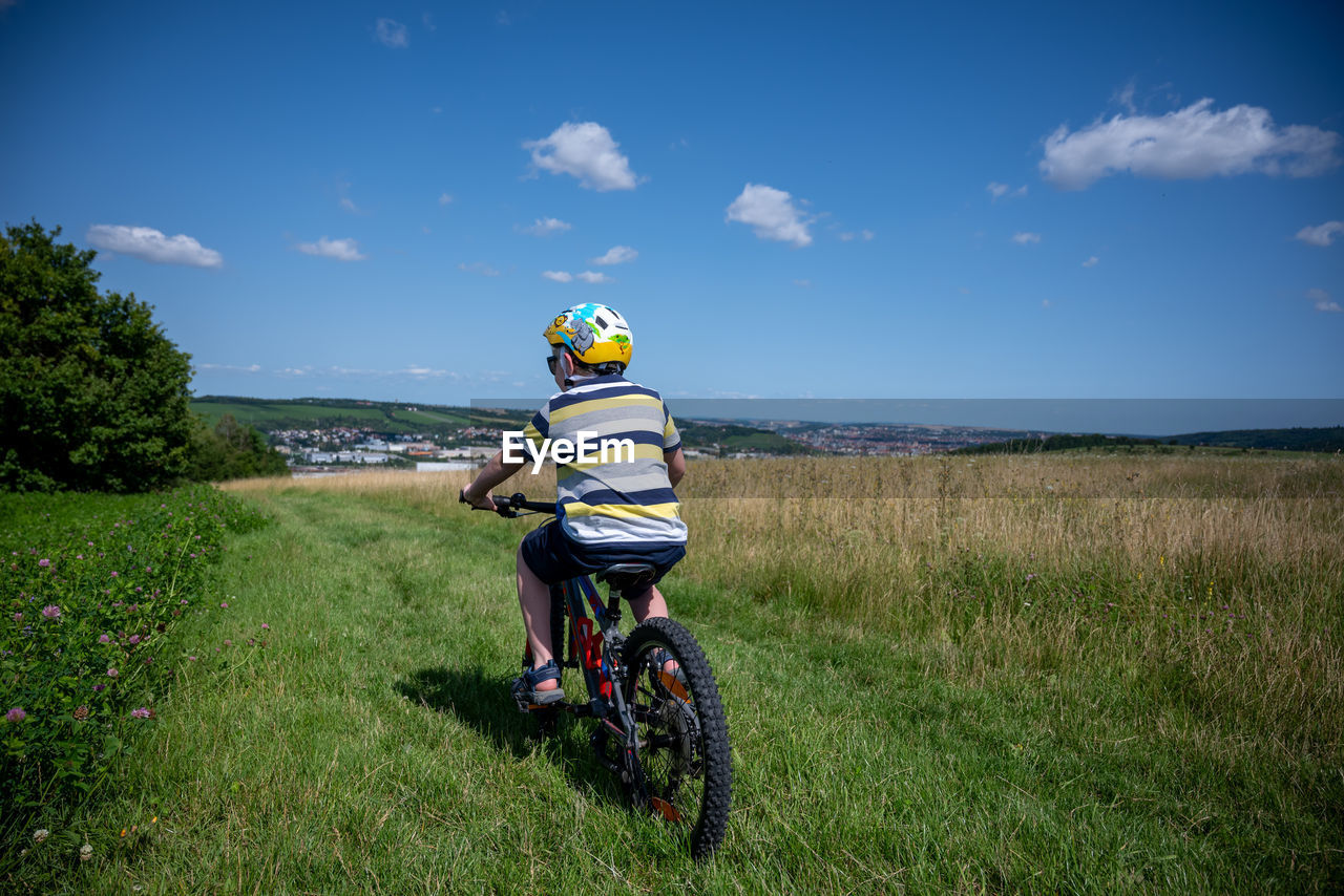 rear view of woman riding bicycle on field against sky