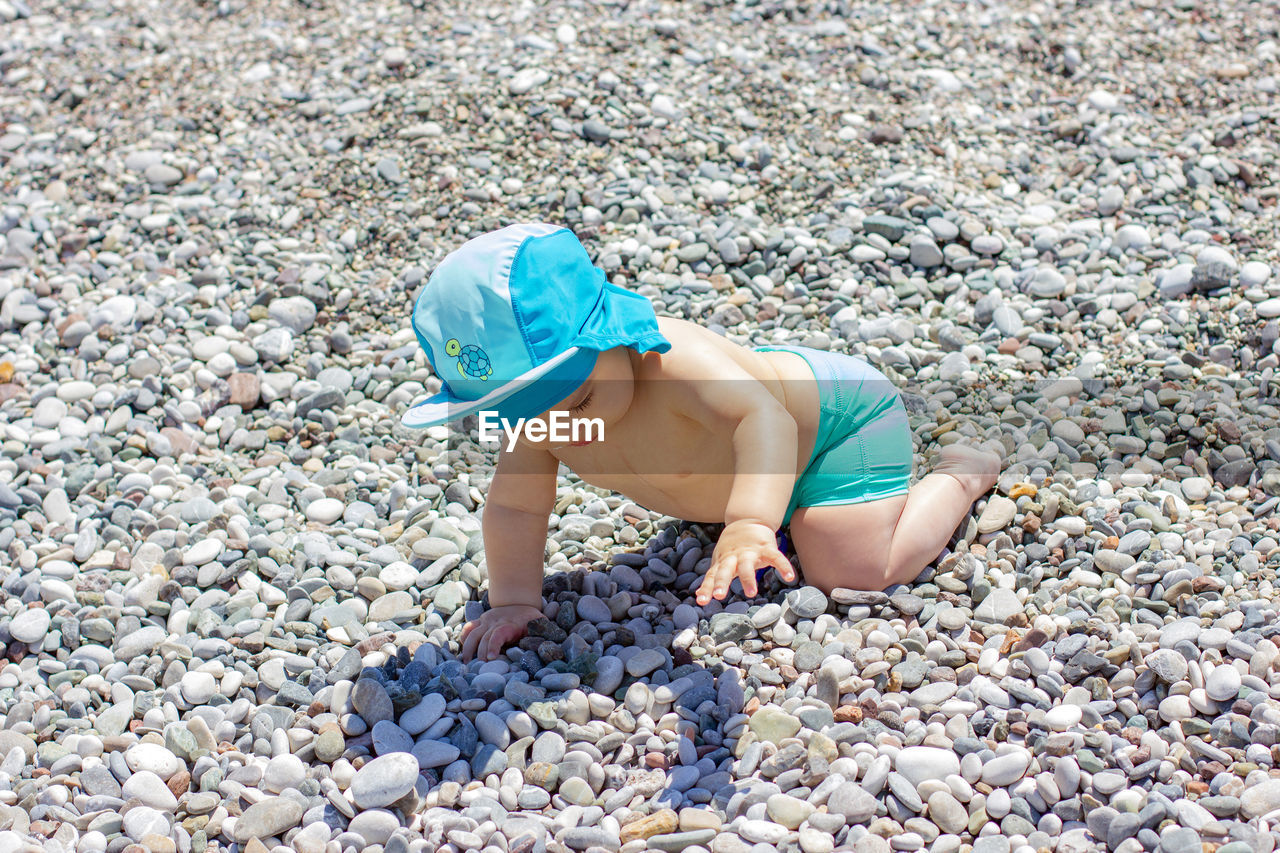 Sweet chubby baby on pebble beach. blue sea and summer sunshine