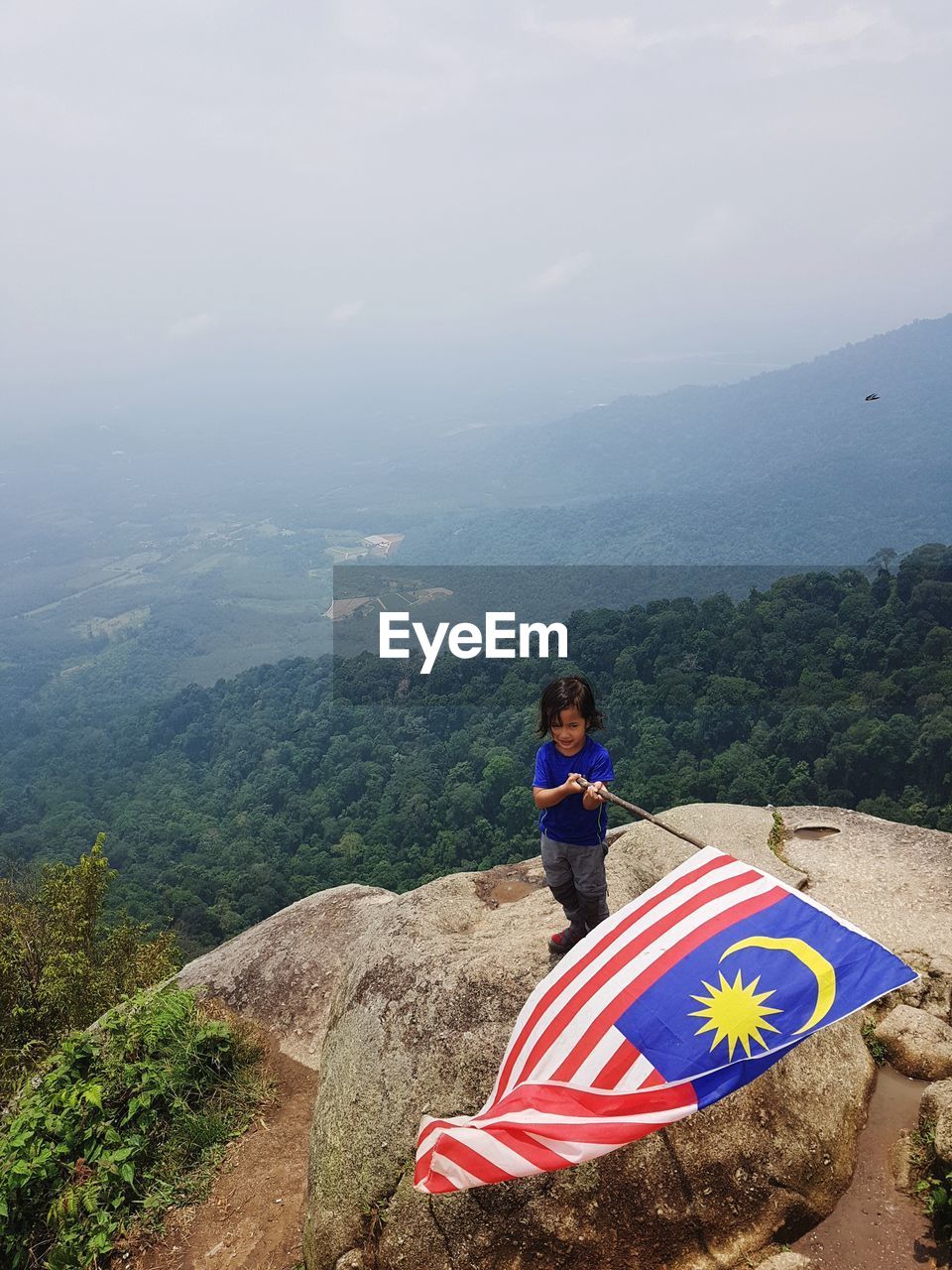 High angle view of boy holding flag while standing on rock against sky