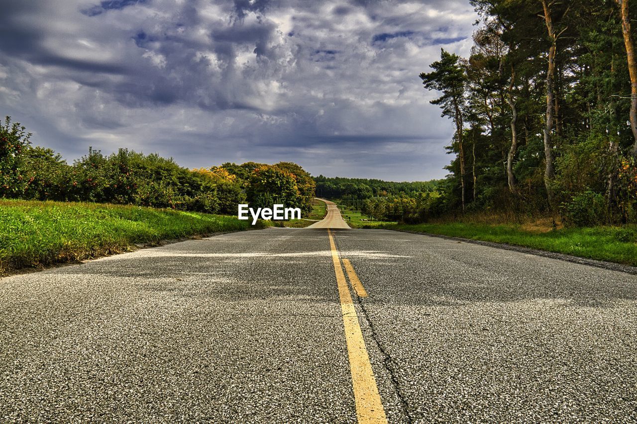 road, sky, transportation, cloud, plant, tree, the way forward, nature, asphalt, landscape, road surface, environment, rural area, no people, grass, symbol, land, road marking, beauty in nature, infrastructure, diminishing perspective, street, scenics - nature, marking, vanishing point, lane, morning, sunlight, horizon, outdoors, tranquility, city, sign, country road, travel, empty road, highway, day, tranquil scene, rural scene, green, tarmac, autumn