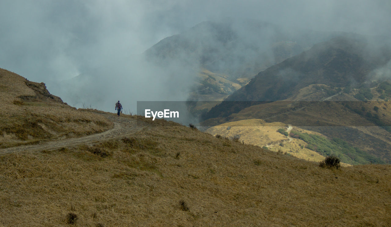 REAR VIEW OF MAN STANDING ON MOUNTAIN