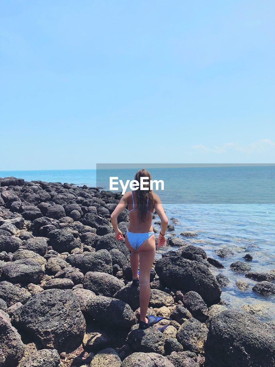 Rear view of woman wearing bikini walking at beach against clear sky