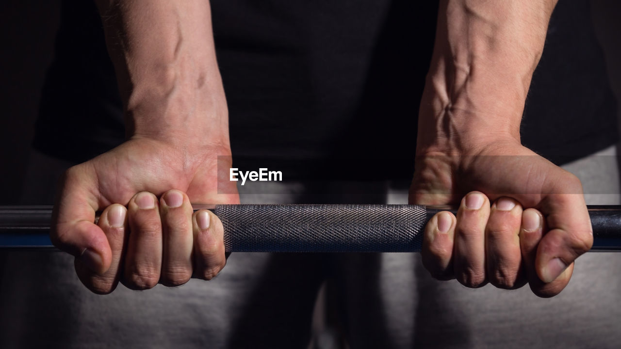 Cropped hands lifting dumbbell in darkroom