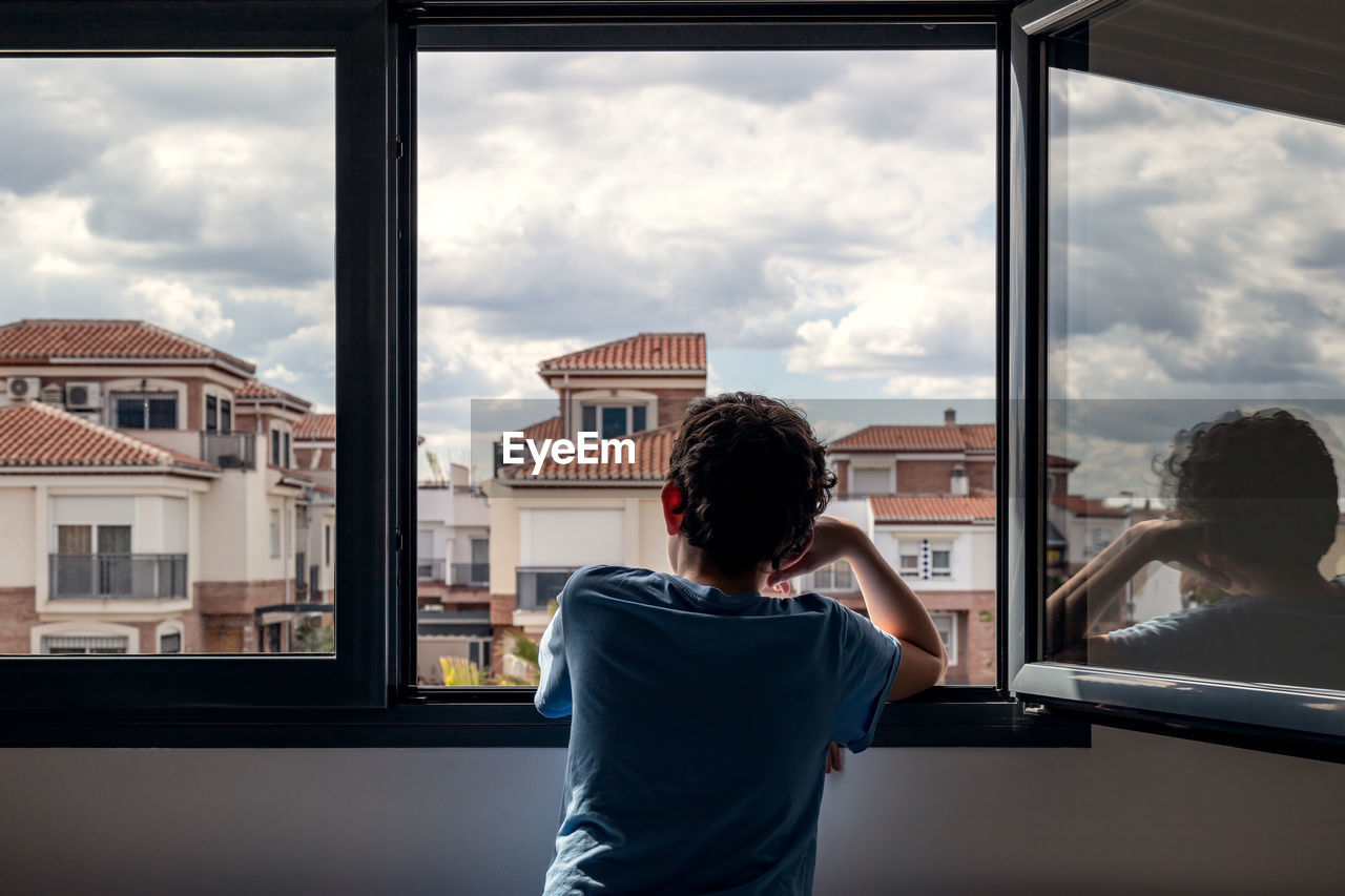 Rear view of boy looking through window at home