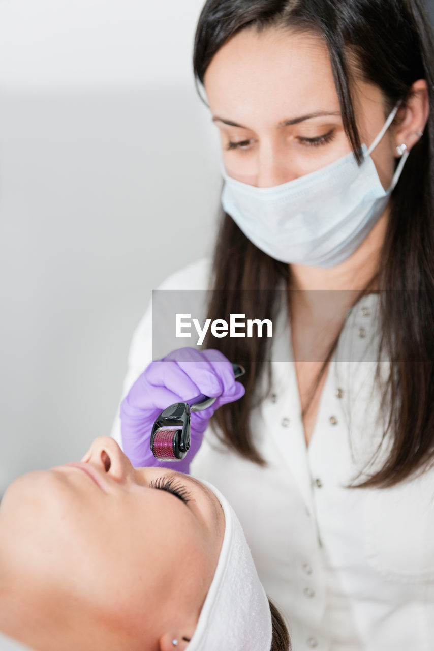 Close-up of woman lying down with while beautician using cosmetic roller on face at spa