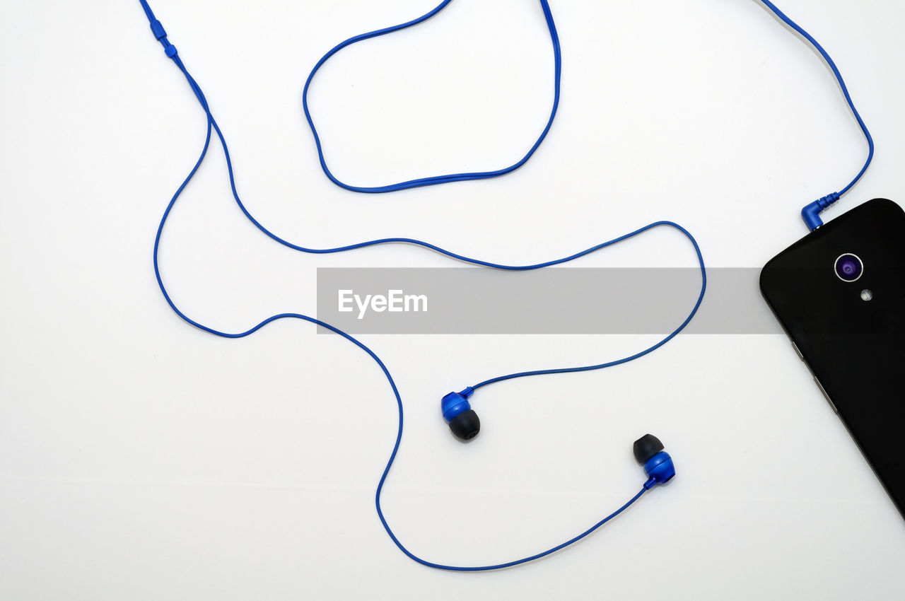 Close-up of mobile phone with in-ear headphones on white background