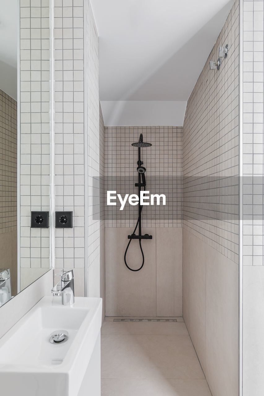 Narrow bathroom with shower zone and small sink. interior of modern bathroom with beige tiles.