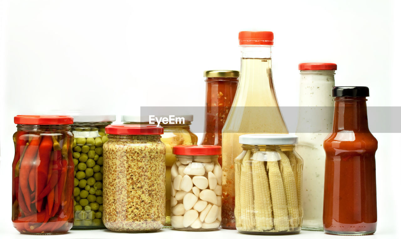 Close-up of various food in jars and bottles against white background