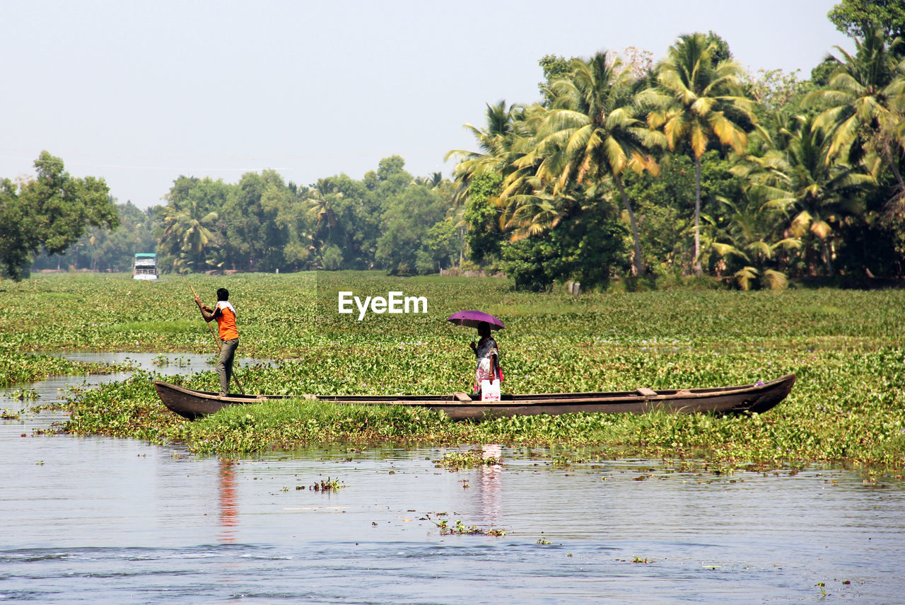 People rowing boat in river against sky