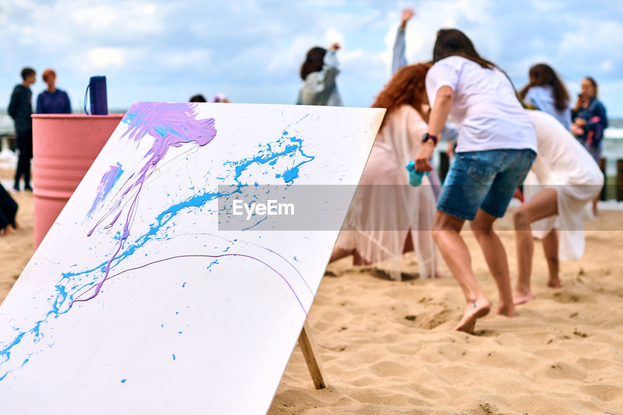 Drip painting outdoor art performance with dancing girls on sandy sea beach. painter artist drawing 