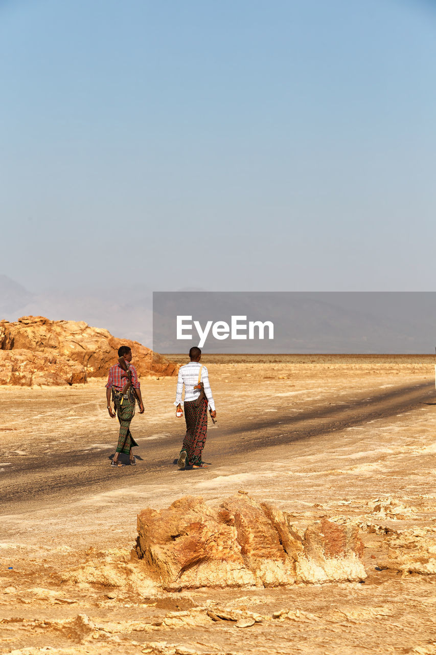 REAR VIEW OF A MEN WALKING ON DESERT