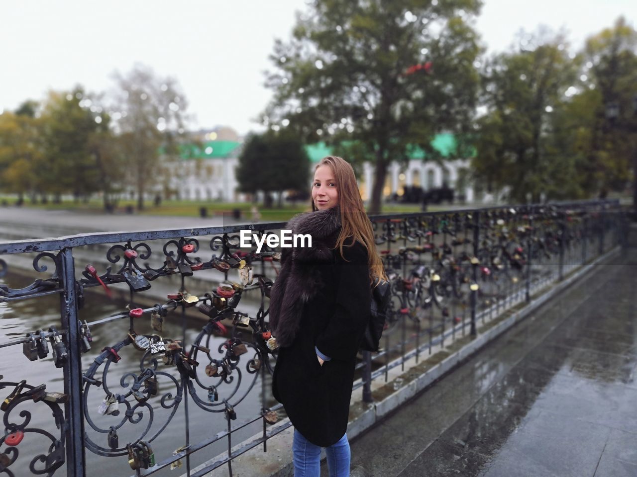 Portrait of smiling woman wearing warm clothing while standing on bridge over canal