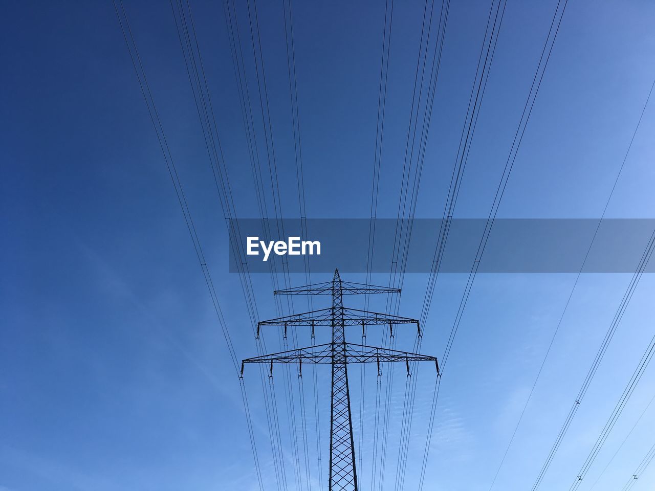 Low angle view of electricity pylon against clear blue sky
