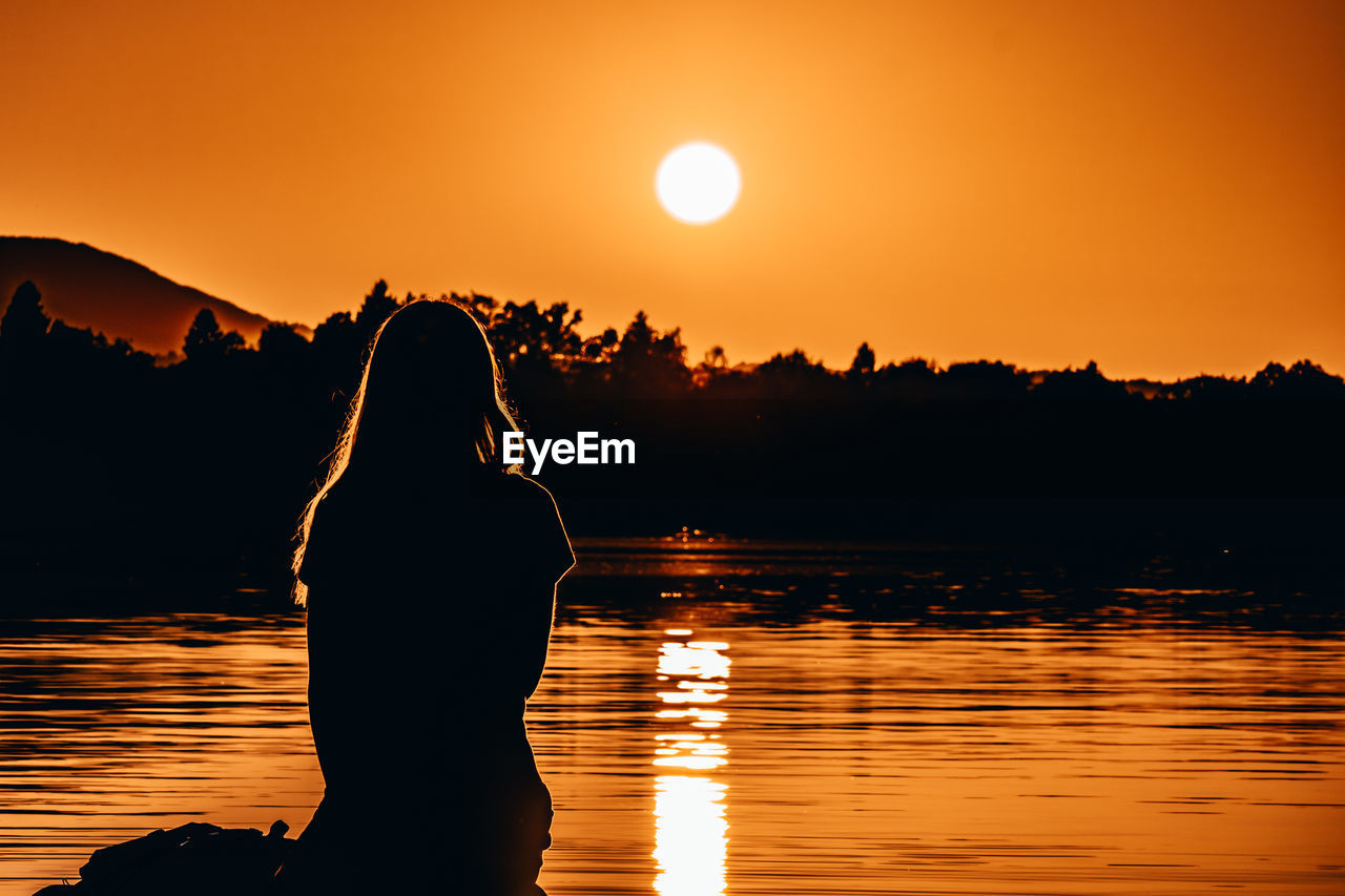 Rear view of silhouette woman standing against sky during sunset