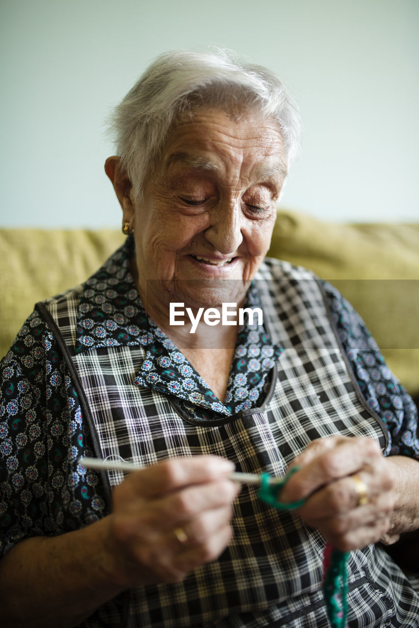 Portrait of smiling senior woman crocheting on the couch at home