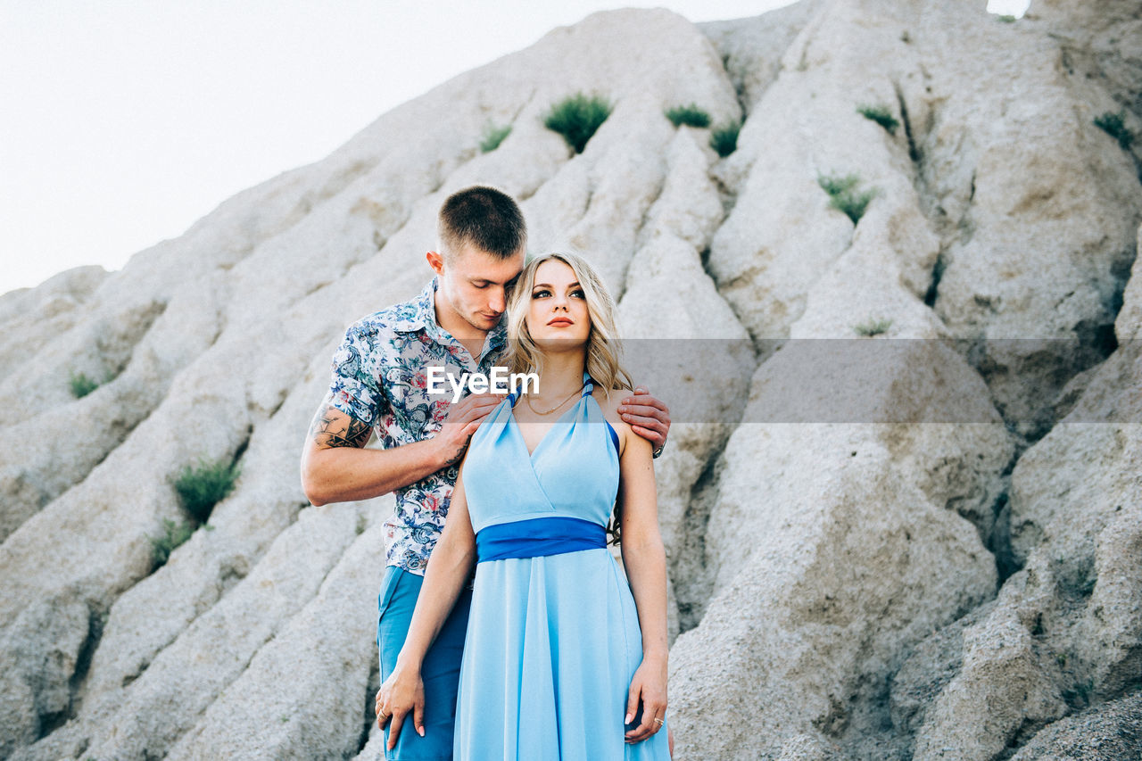 YOUNG COUPLE STANDING ON ROCK AT SHORE