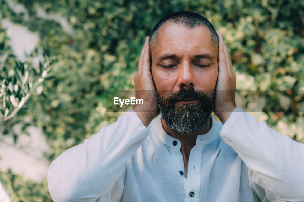 Man sitting with his eyes closed and doing a reiki auto treatment, holding hands on ears.